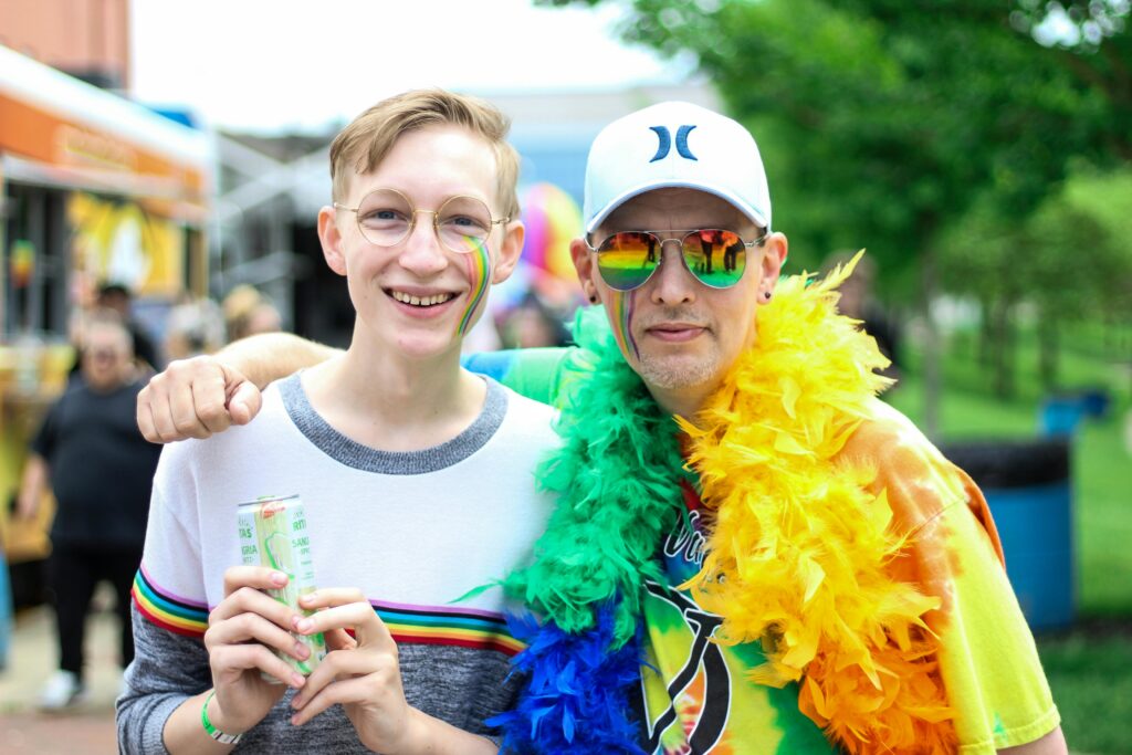 pexels-photo-2306806-2306806 Two people smiling and embracing at a vibrant outdoor pride festival with rainbow colors.